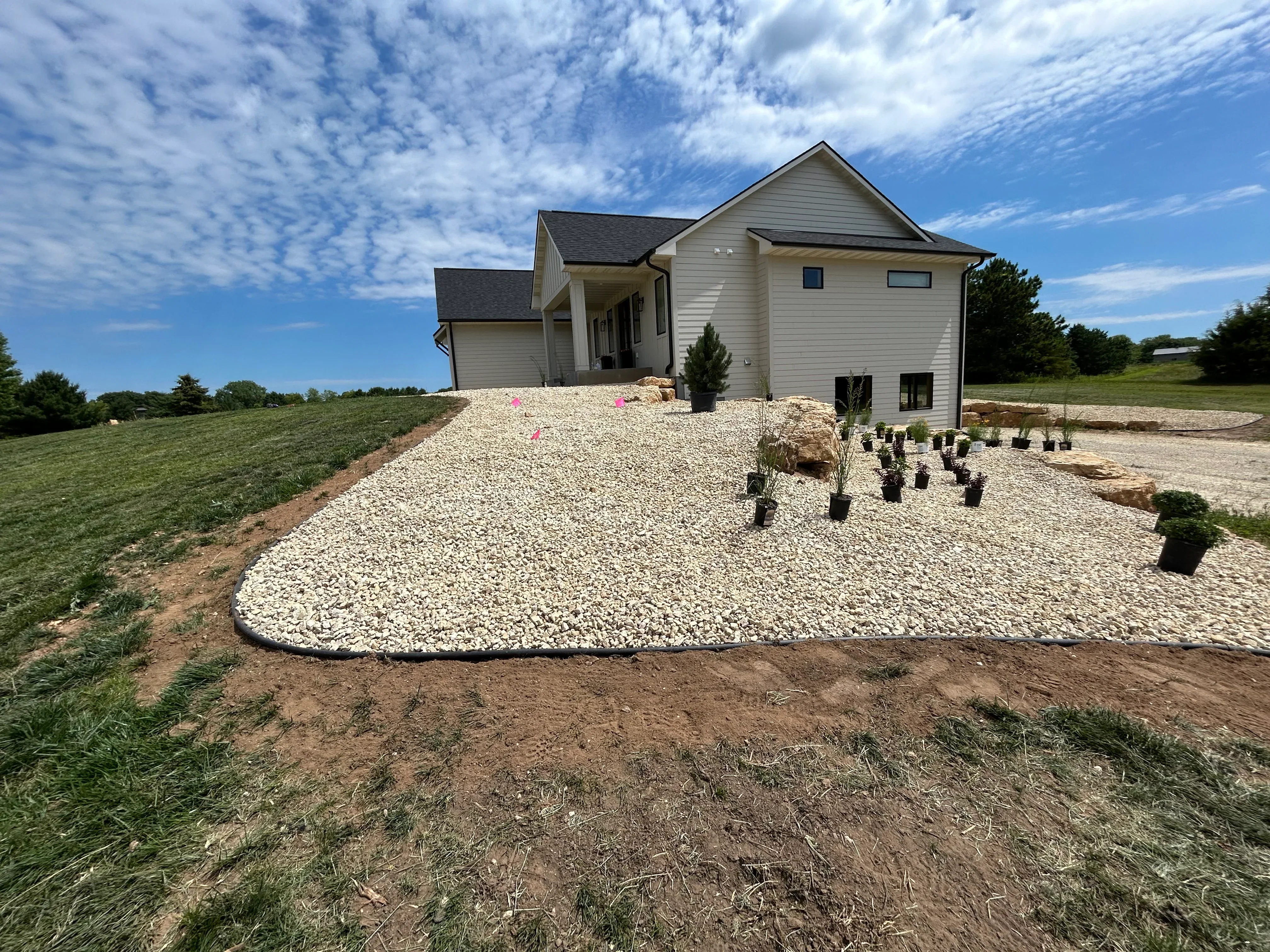 New home with white vinyl siding and crushed stone driveway on graded lot with landscaping