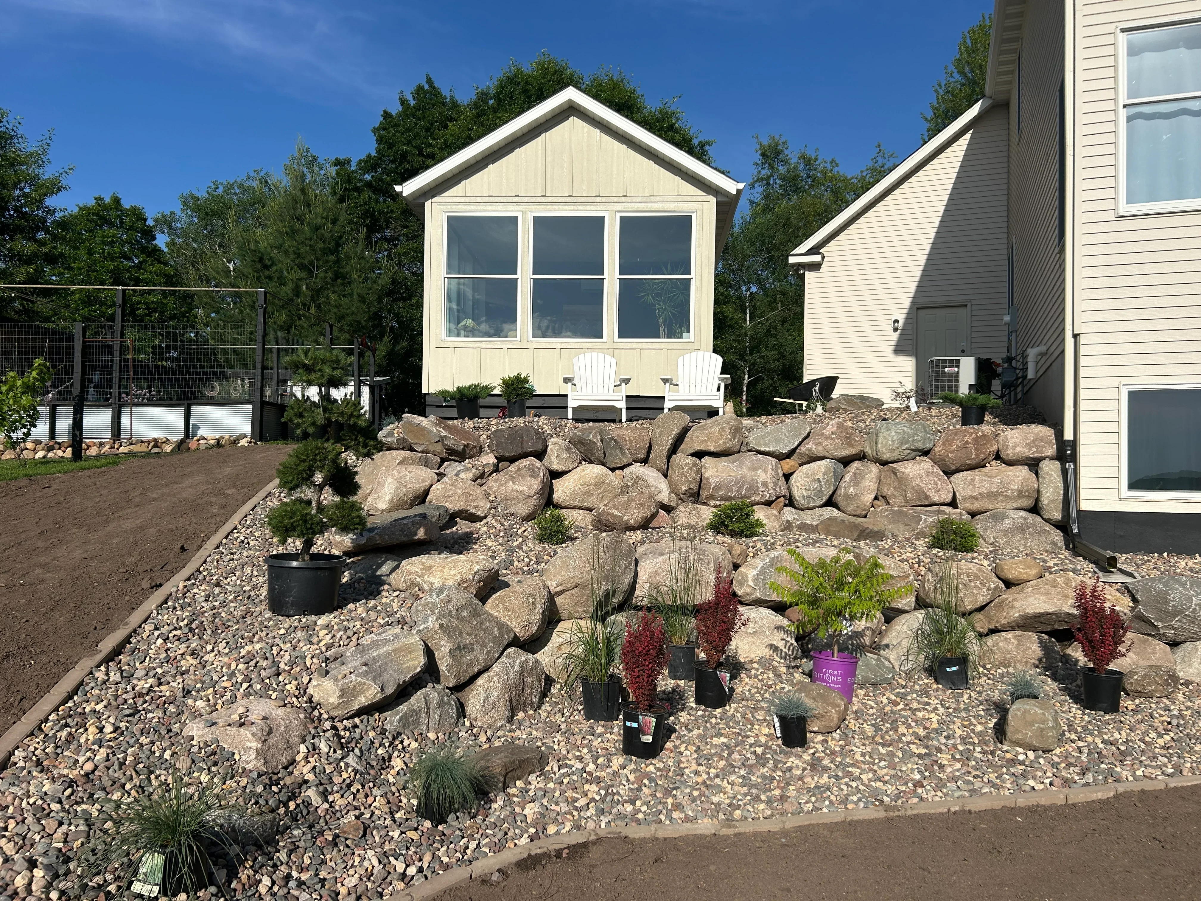 Stacked stone retaining wall with gravel landscaping and newly planted shrubs in residential backyard