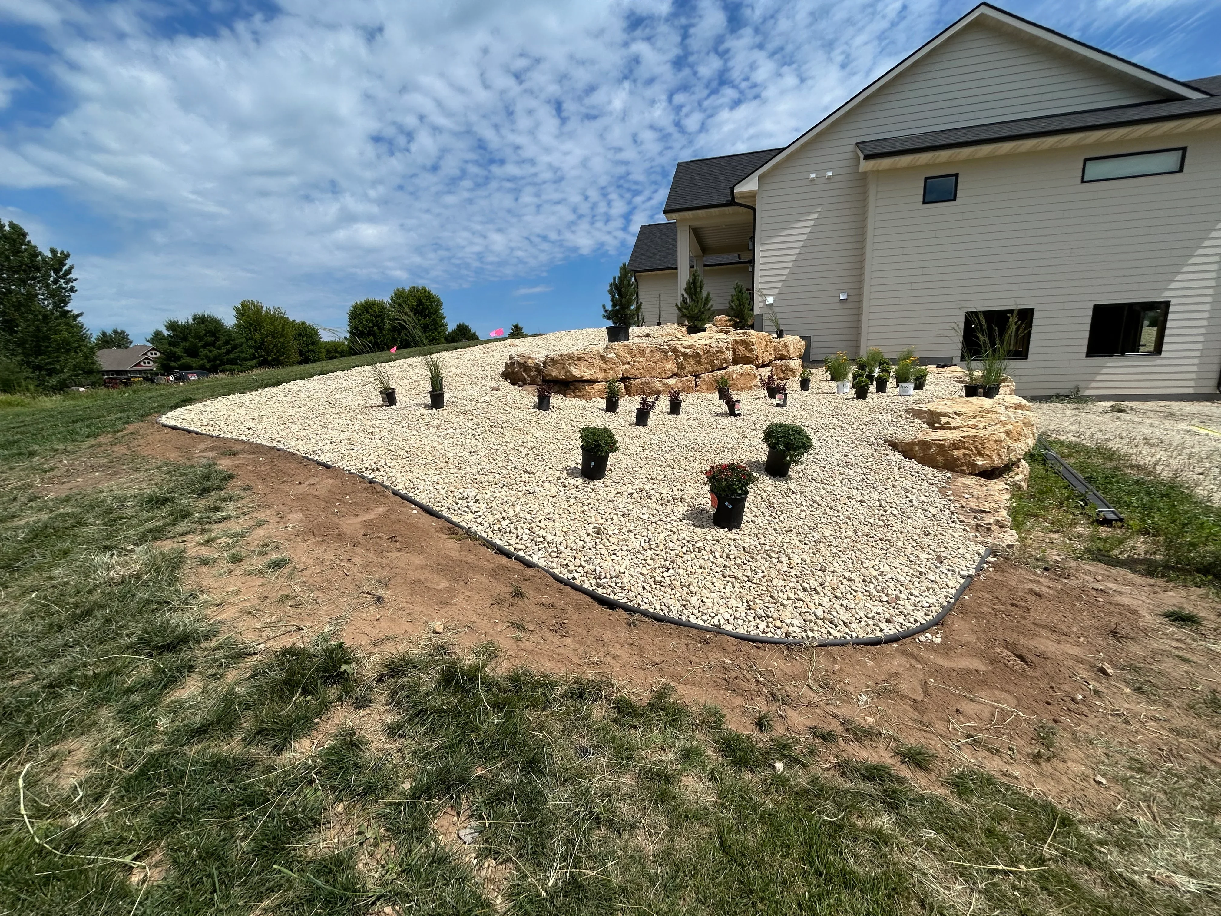 Residential yard with graded white river rock landscape, stone features, and planted shrubs