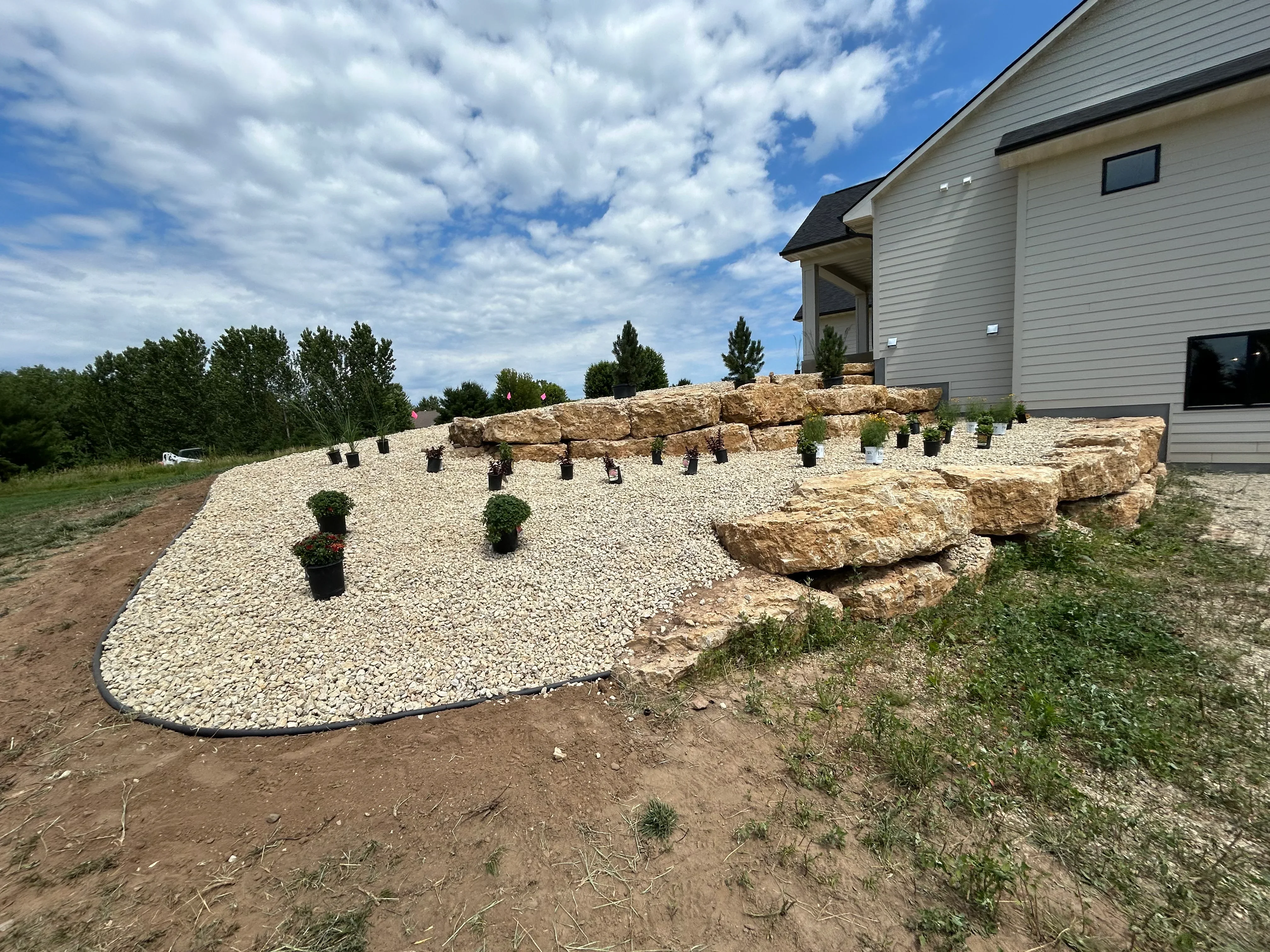 Residential landscape with gravel base, stone retaining wall, and newly planted vegetation