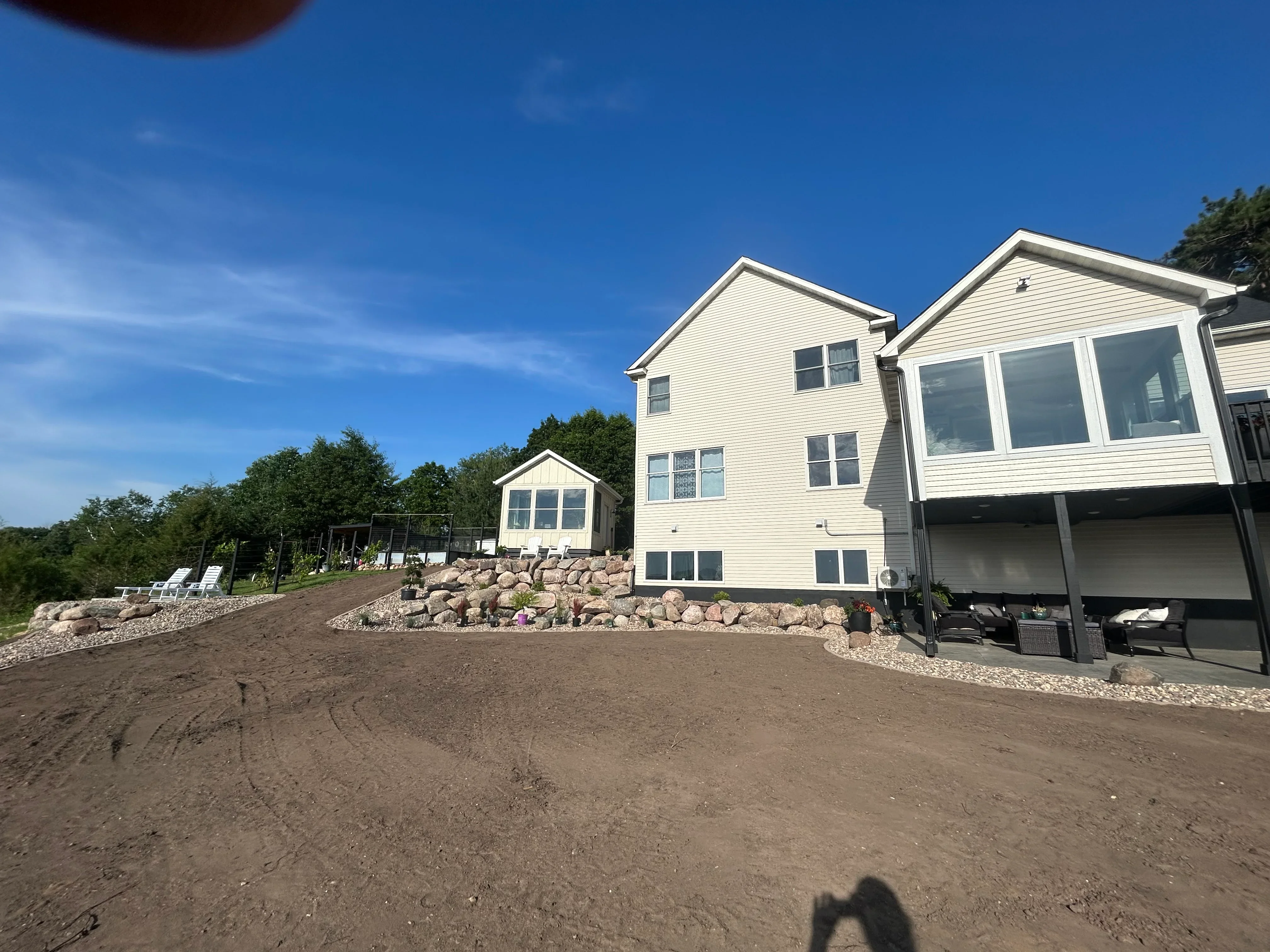 White two-story home with excavated driveway, boulder retaining wall, and gravel landscaping