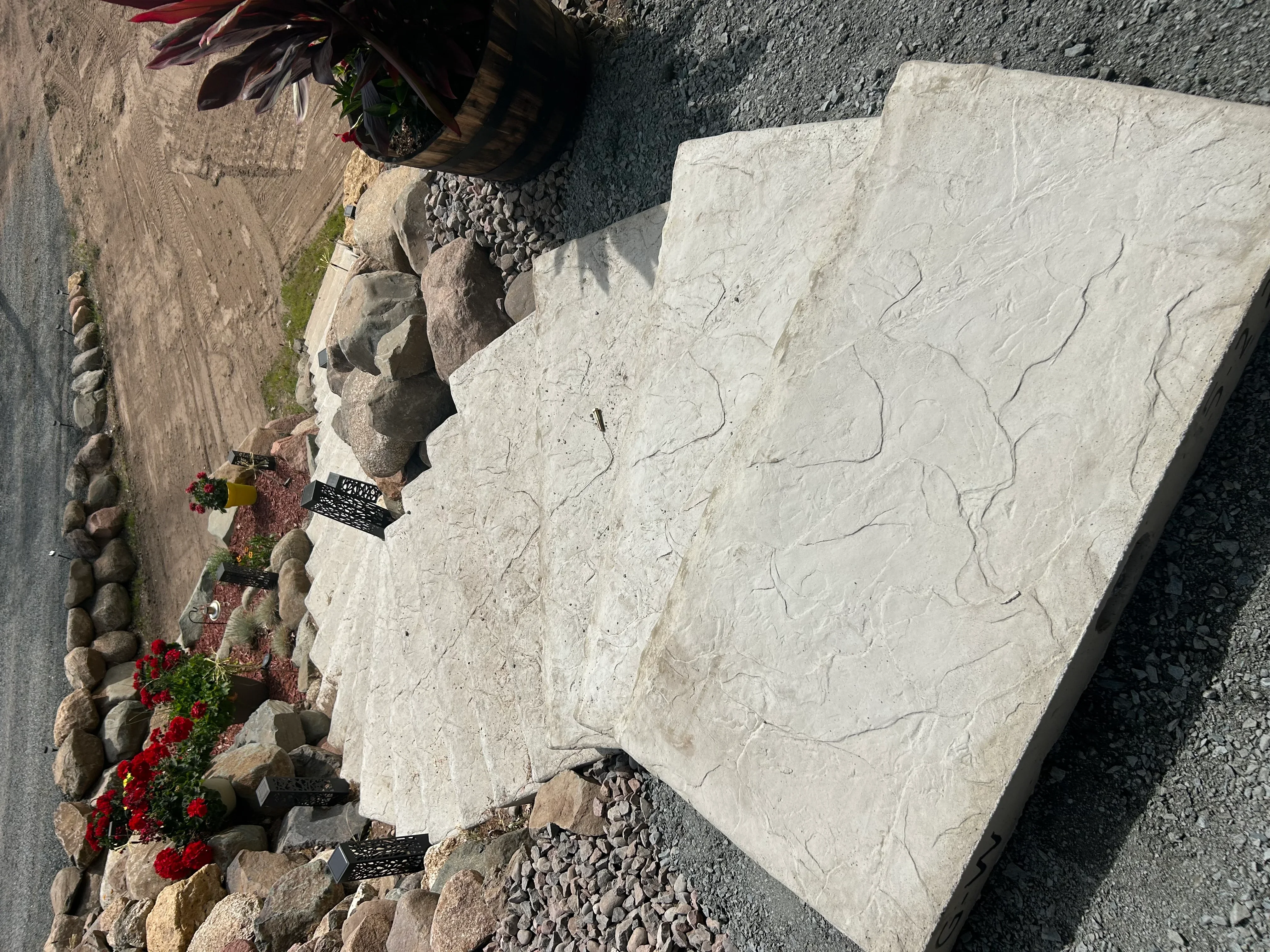 Cream stone patio with textured finish, stone edging, and red flowering plants
