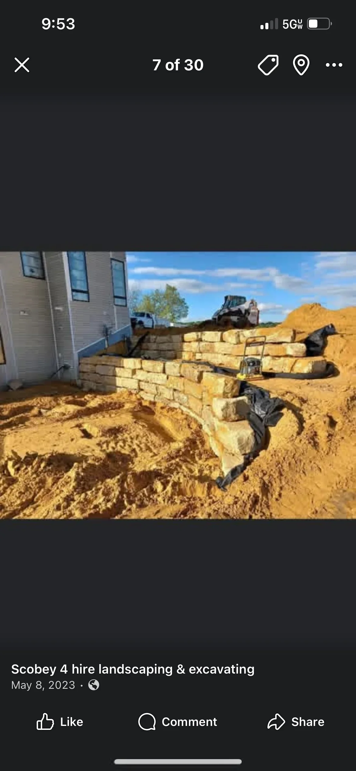 Stone retaining wall construction with excavator and graded earth on residential property