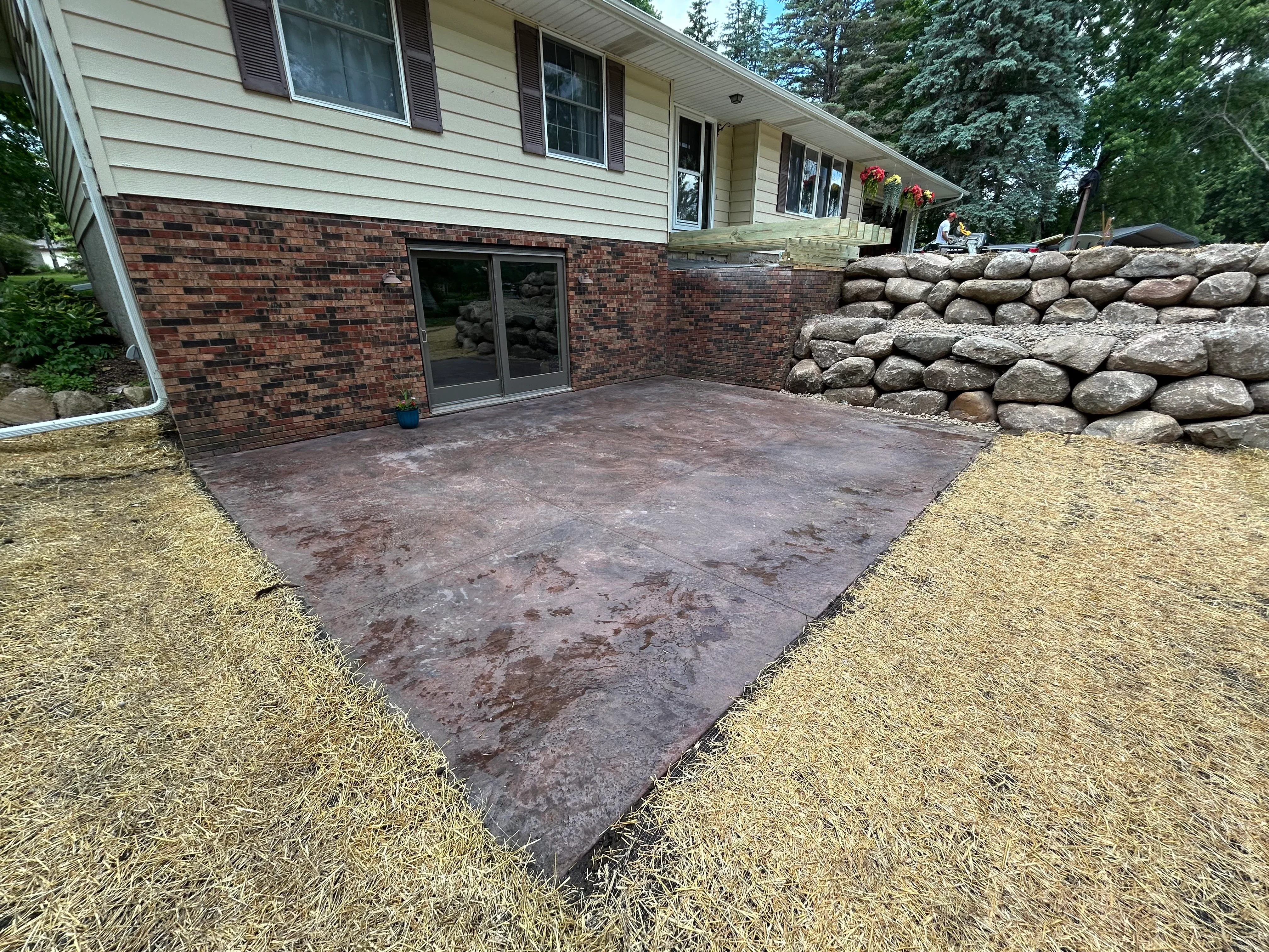 Prepared patio base with graded soil and stone retaining wall behind brick home