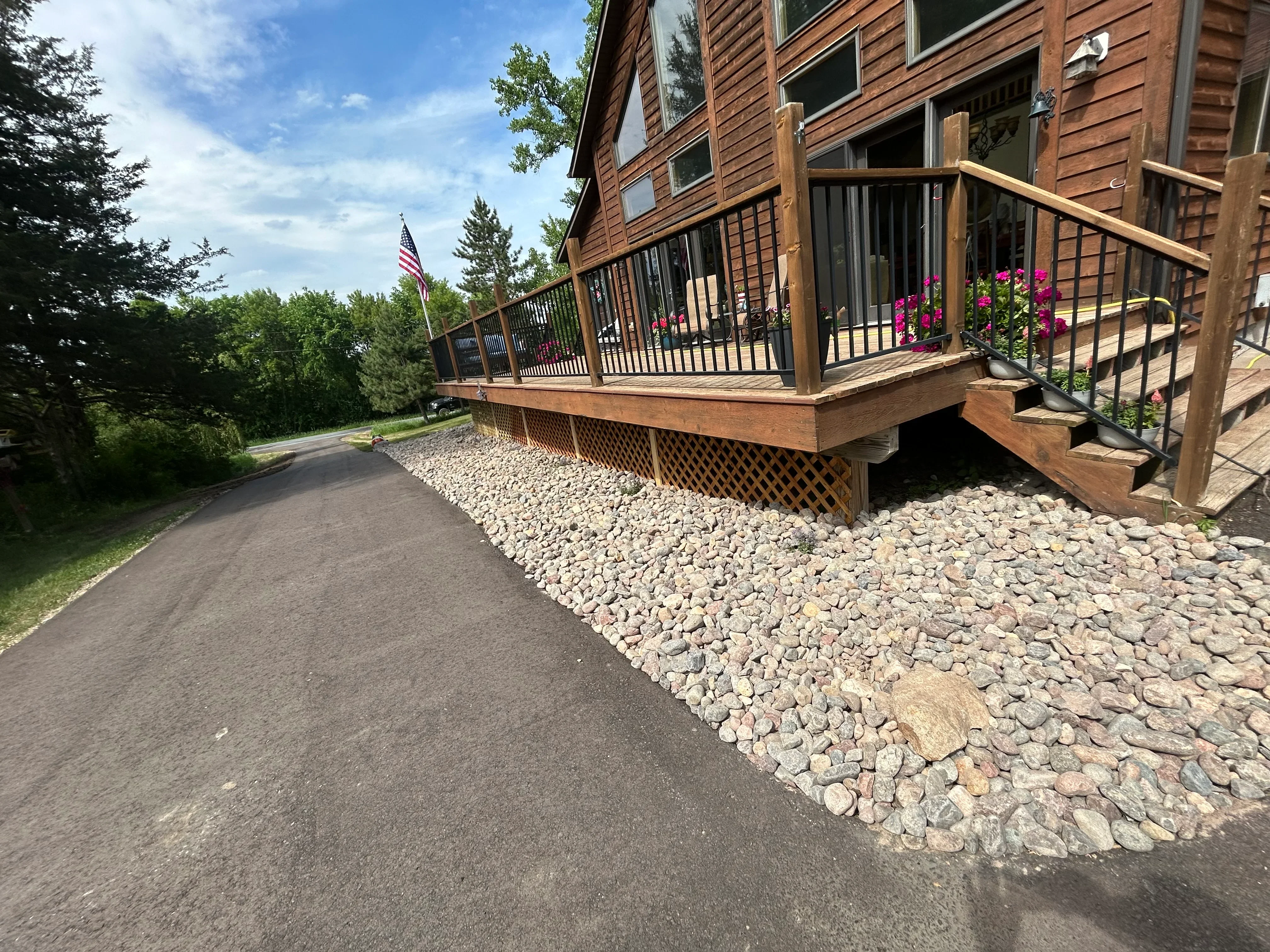 Newly paved asphalt driveway with river rock landscaping beside wooden deck