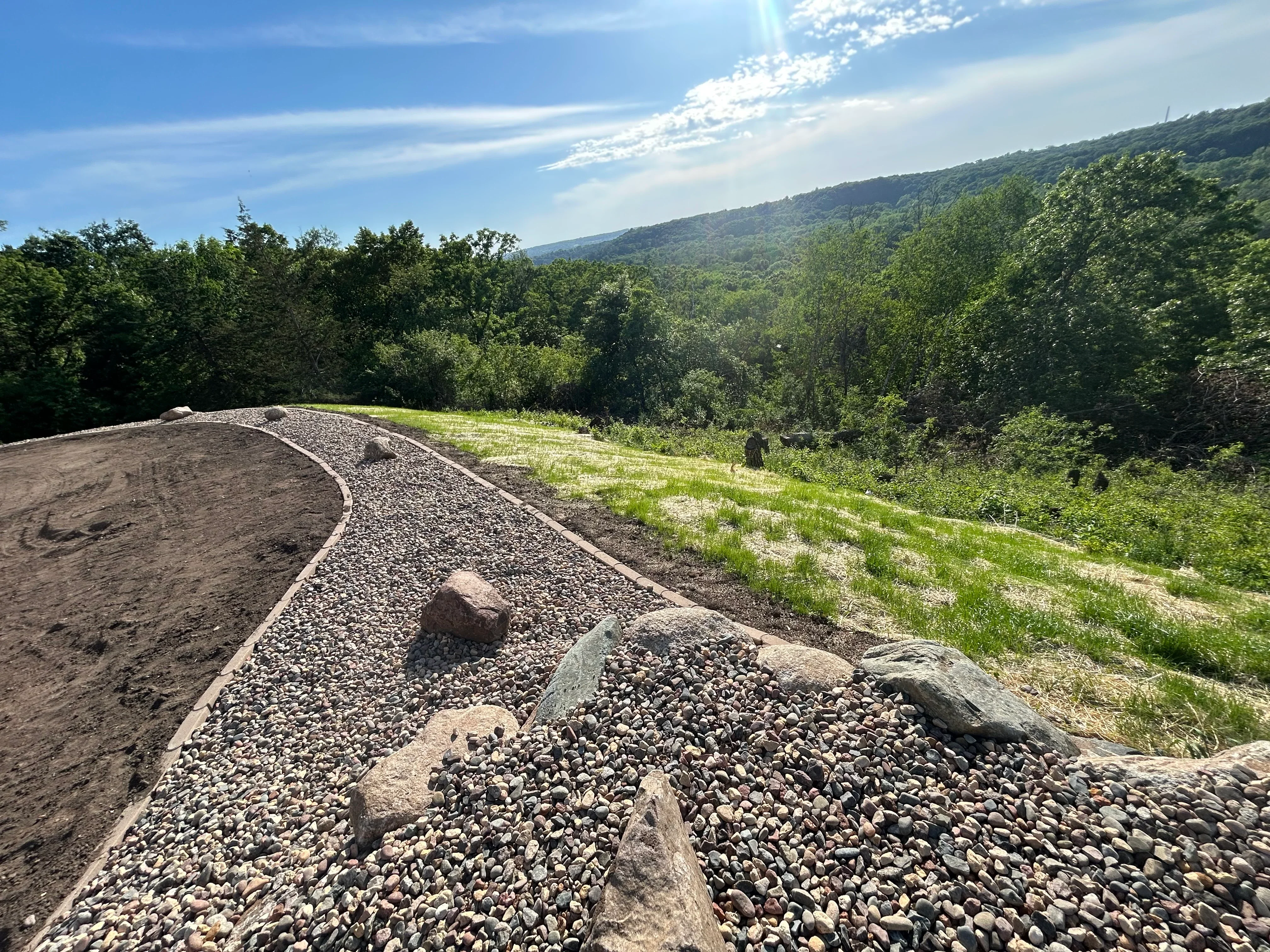 Hillside excavation with gravel drainage path and forest landscape in Hudson, WI