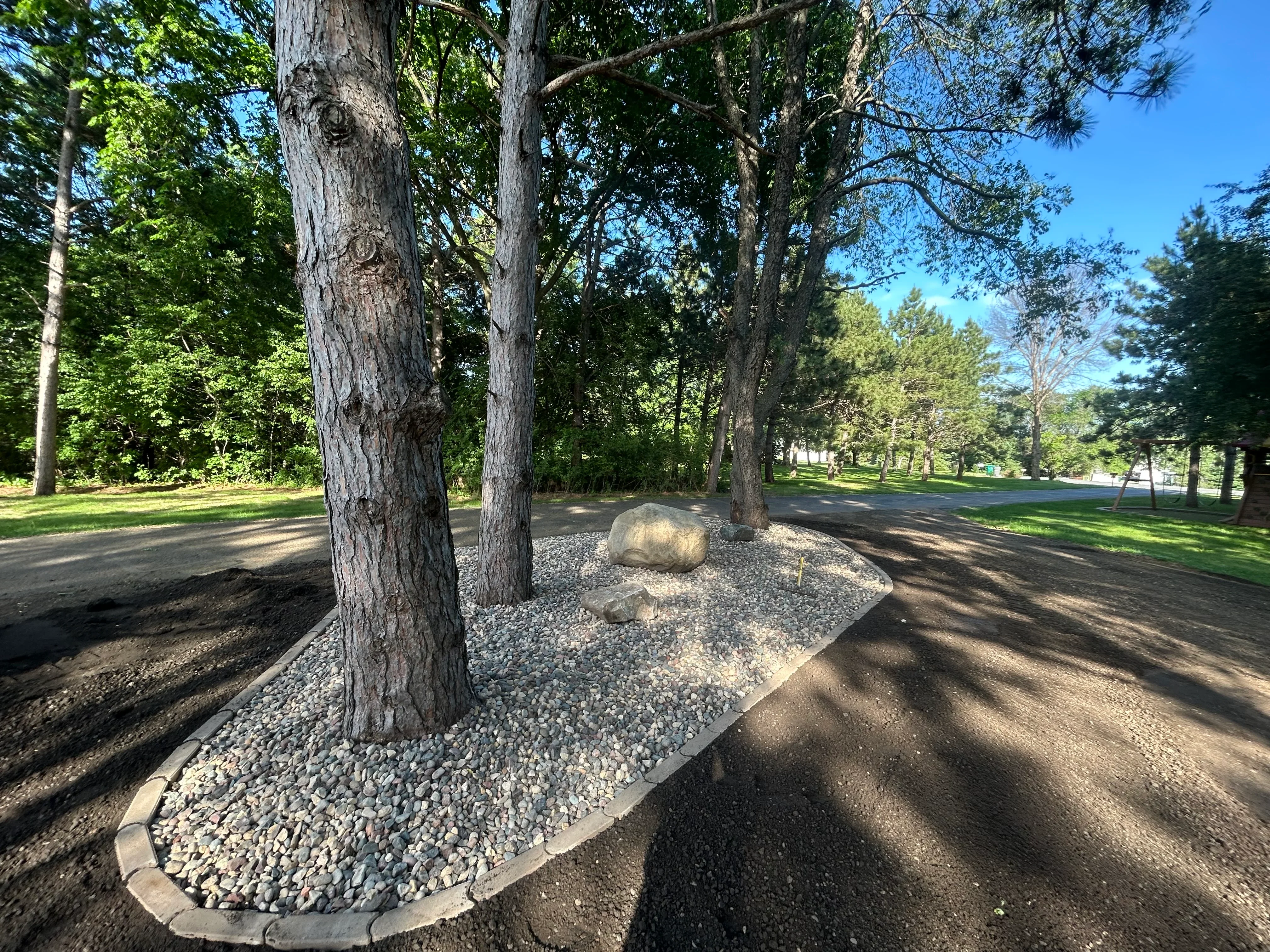 Excavated tree base with gravel infill and landscape edging around mature trees