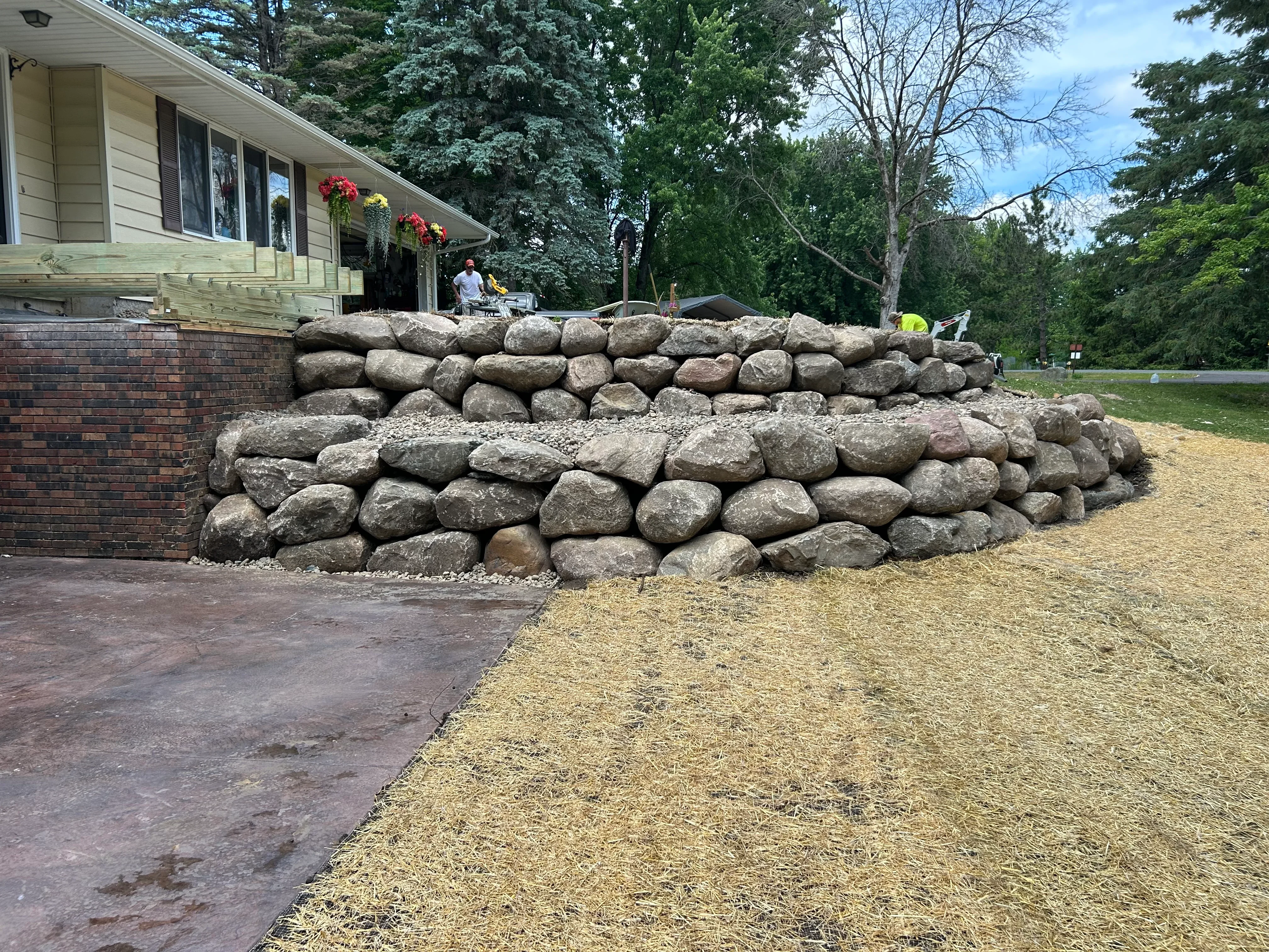 Stacked granite boulder retaining wall with gravel base beside residential home