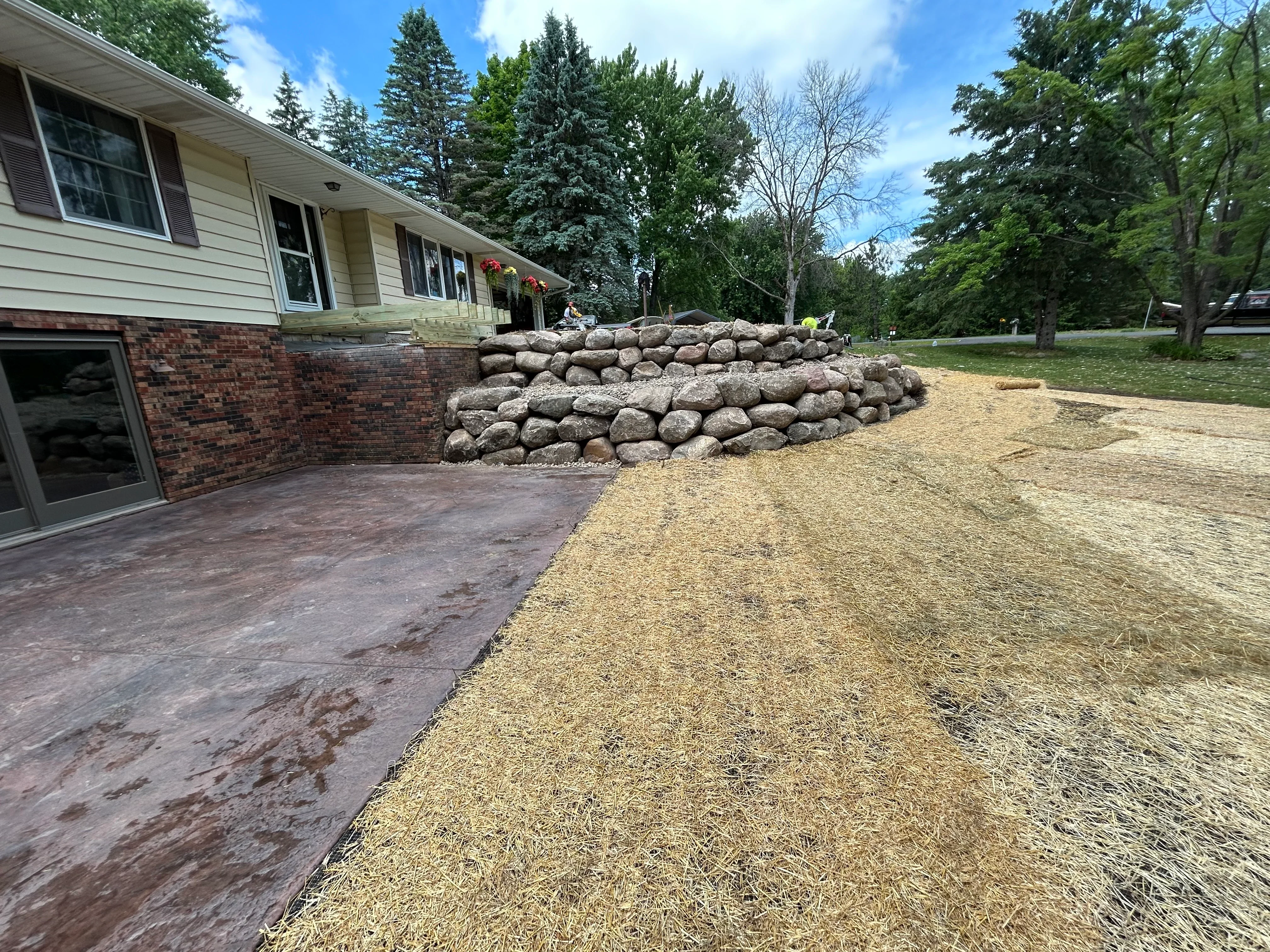 Residential driveway with gravel surface and stacked stone retaining wall beside brick home