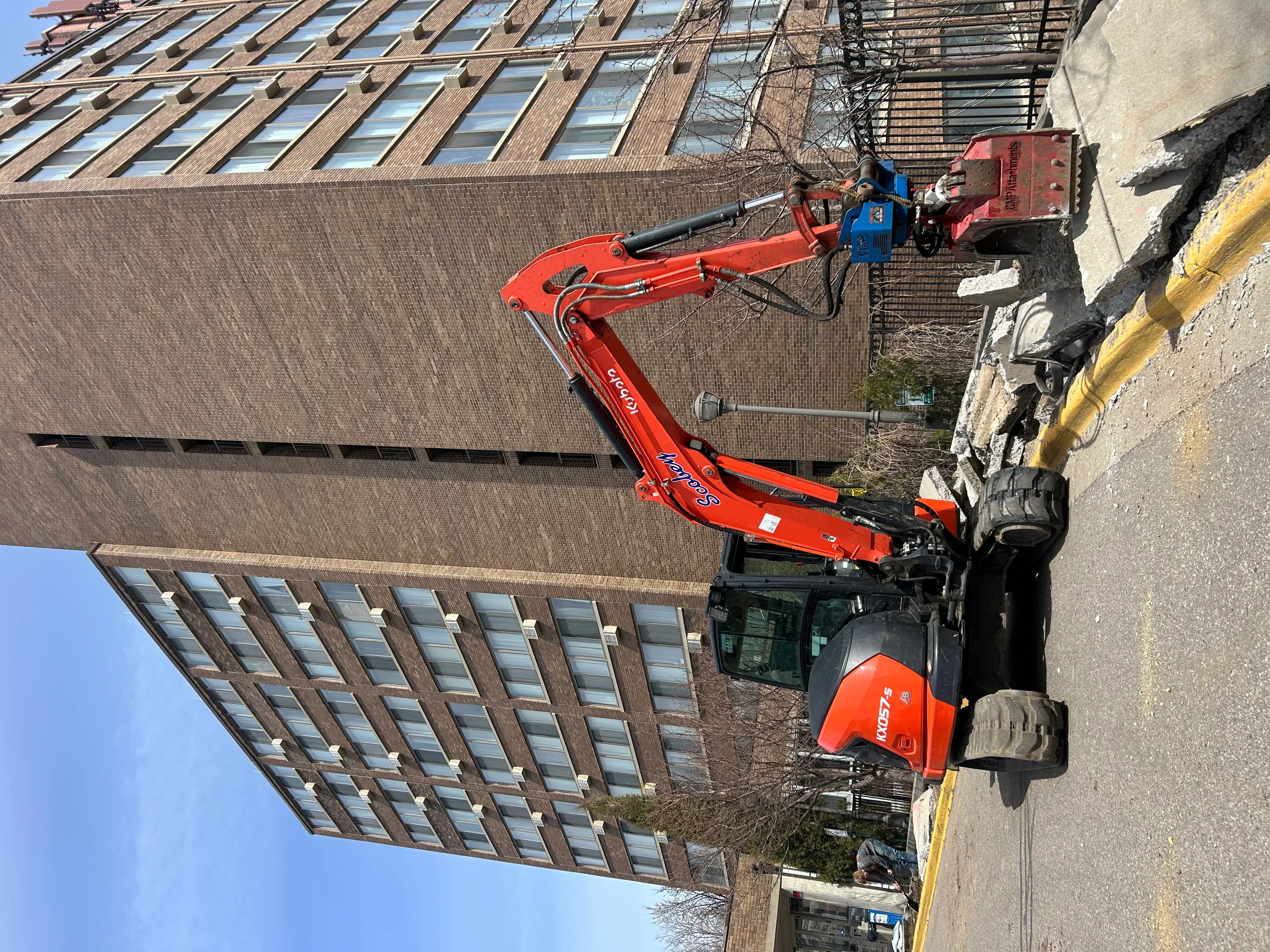 Red hydraulic excavator with boom arm performing building demolition on brick structure
