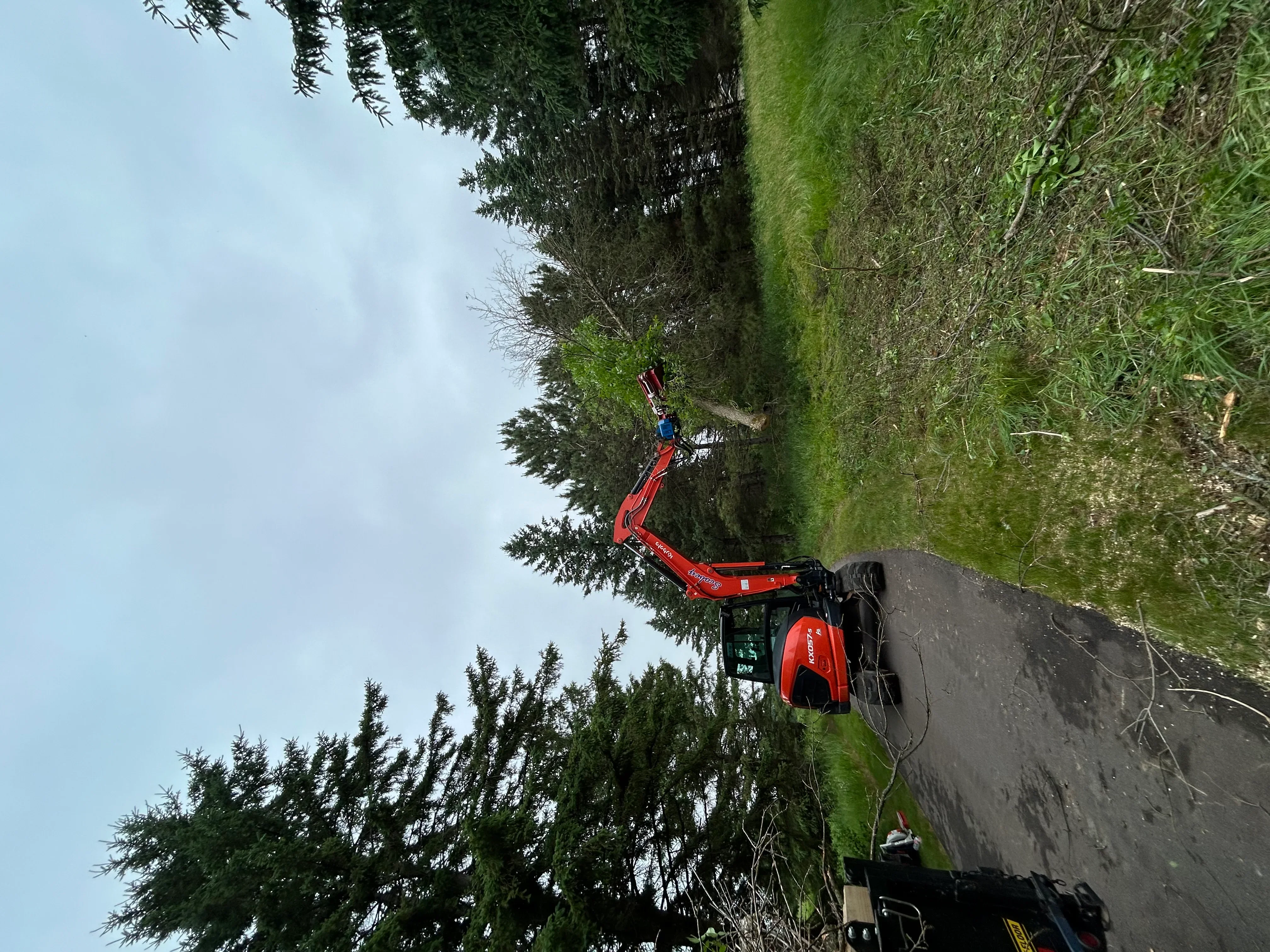 Red excavator on residential property with graded soil and green grass