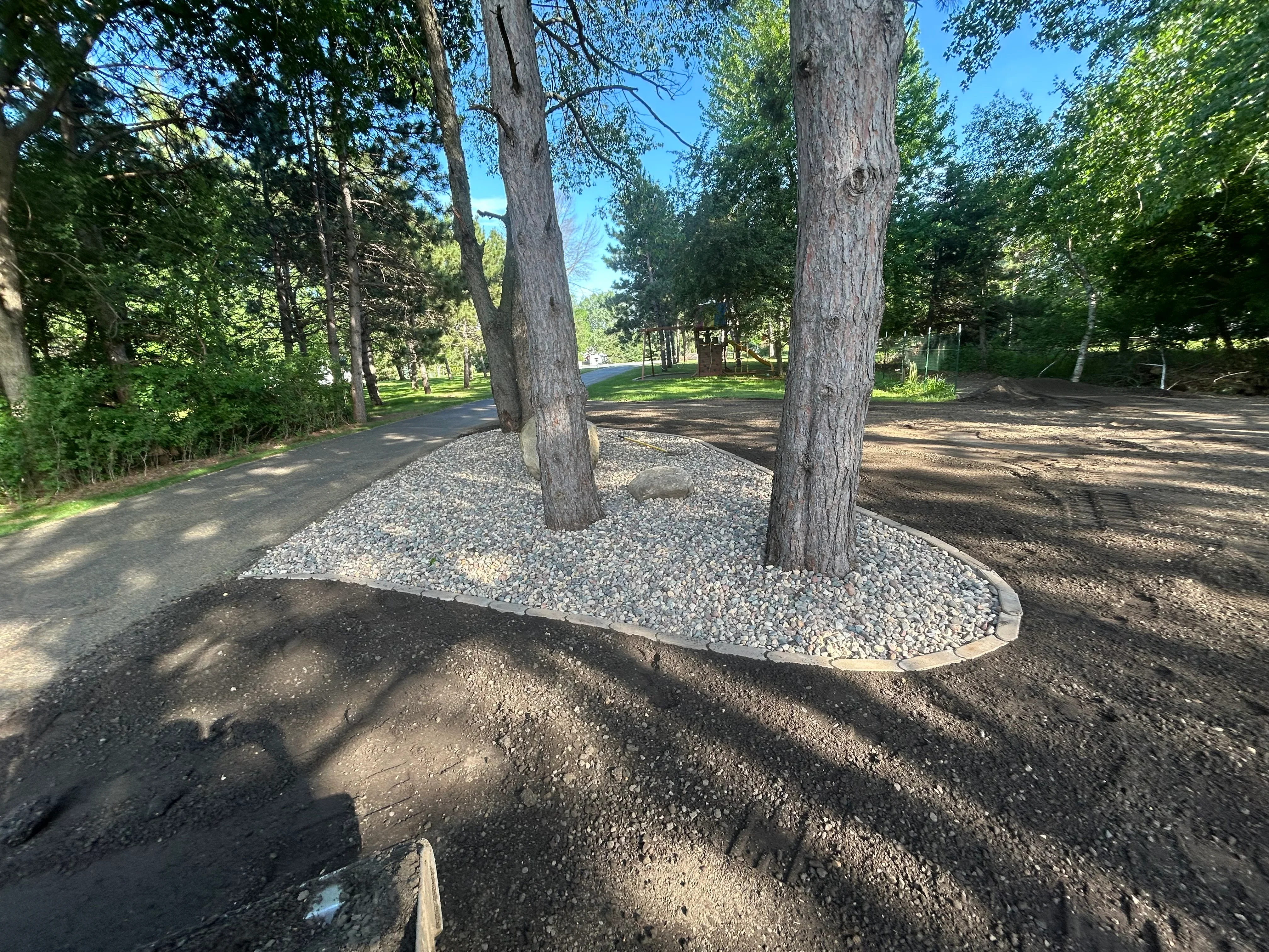 Gravel tree base with metal edging around two large trees in park landscape